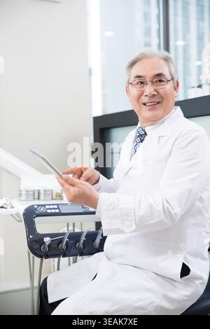 Smiling confident senior dentist using an electric tablet Stock Photo