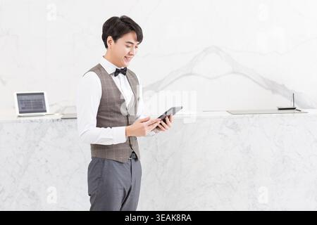 A young man in a business attire smiles as he checks his tablet in a modern, minimalist office. Stock Photo