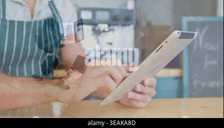 Tapping barista wearing striped apron using tablet behind wooden counter, receipt overlay, espresso. Cafe, coffee, device, terminal, chalkboard, menu, Stock Photo