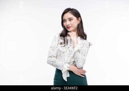 A young Asian woman in a white blouse and dark skirt, posing with her hand on her hip, in a neutral setting. Stock Photo