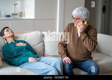 Worried concerned senior husband urgently calling to ambulance while wife having heart attack. Stock Photo