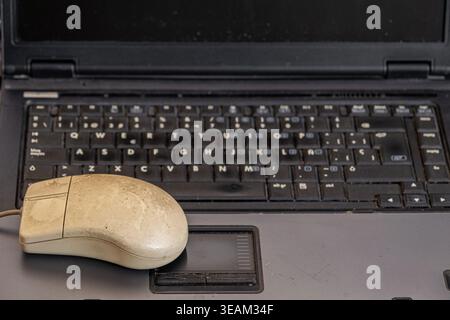 a vintage, worn-out serial mouse, from the 1990s, placed on top of a laptop keyboard Stock Photo