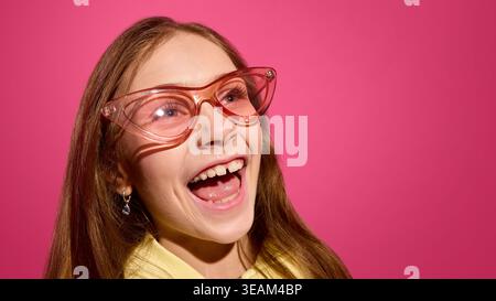 Excited child girl laughing in pink glasses in studio pink background expressive emotion concept Stock Photo