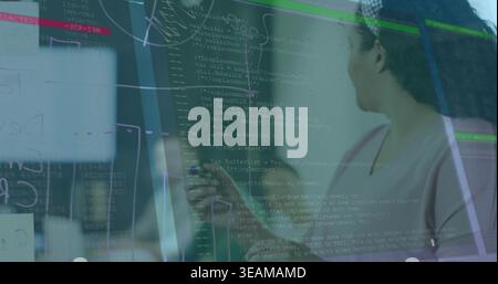 Standing woman wearing light pink top holding marker on glass board in office, code, copy space. Collaboration, teamwork, brainstorming, diagrams, not Stock Photo