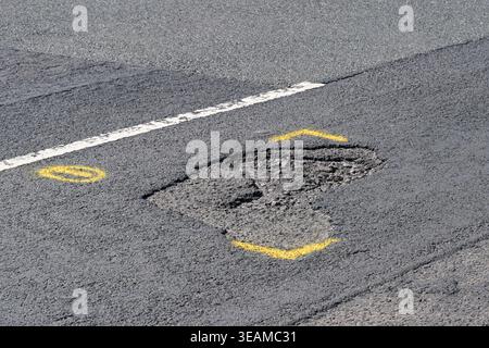 Pothole on a main road through a residential area marked out with yellow paint for repair. No people. Stock Photo