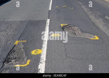 Potholes on a main road through a residential area marked out with yellow paint for repair. No people. Stock Photo