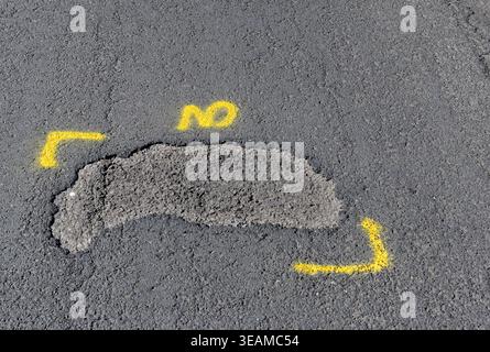 Pothole on a main road through a residential area marked out with yellow paint for repair. No people. Stock Photo