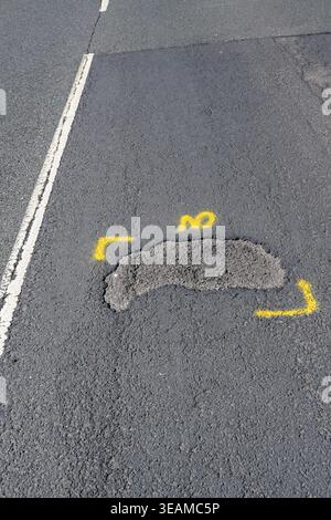 Pothole on a main road through a residential area marked out with yellow paint for repair. No people. Stock Photo