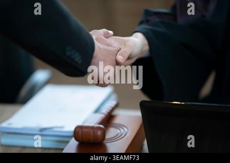 Two business professionals shaking hands over a desk in a formal office setting. Stock Photo