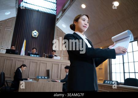 A female lawyer stands confidently in a courtroom, reviewing a document with a serious expression. Stock Photo