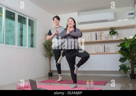 Asian couple doing yoga tree pose at home, wellness fitness Stock Photo