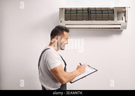 Air conditioner technician inspecting an indoor unit and writing on a clipboard Stock Photo