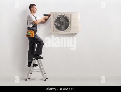 Technician installing an air conditioning unit on a wall with a drilling machine Stock Photo