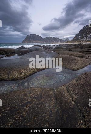 Waves gently crash on unique rock formations under a moody sky at Uttakleiv Beach in Lofoten, Norway. This serene spot is perfect for nature lovers. Stock Photo