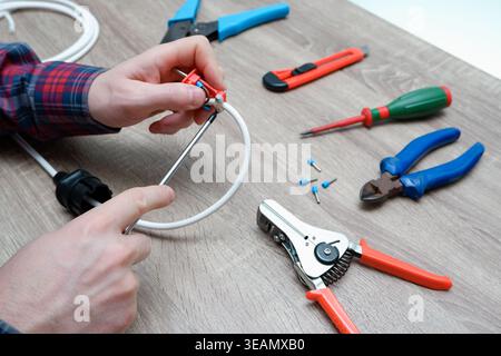 A male electrician changes the plug on an electric wire. Working with electrical tools. Stripper, crimp, screwdriver, wire cutters. Stock Photo