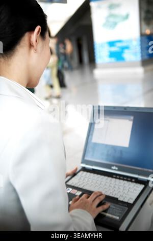 A man sits at a table in a public area, working on a laptop. Stock Photo