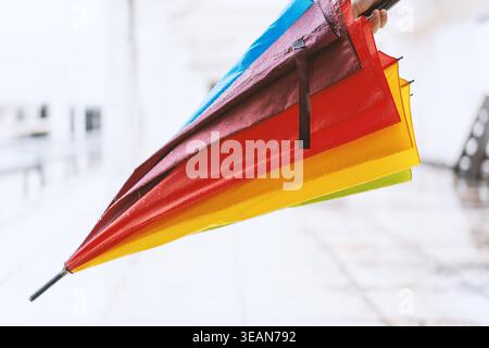 Colorful rainbow umbrella held upside down in snowy winter scene, vibrant contrast against white Stock Photo