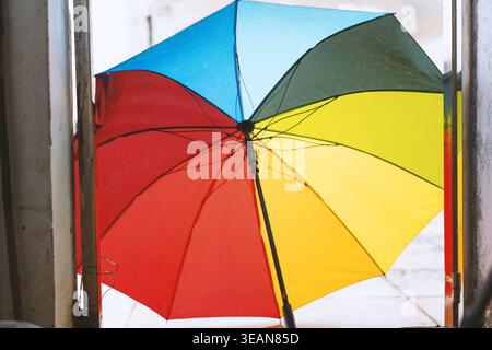 Colorful rainbow umbrella displayed indoors near window, vibrant sections of blue, red, green, and Stock Photo