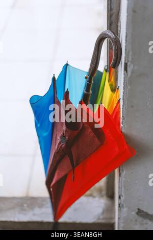 Colorful folded umbrellas hanging by a window frame, vibrant rainbow hues against concrete and tile Stock Photo