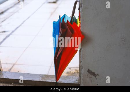 Colorful umbrella hanging on concrete wall beside wet pavement, urban street scene with rain-soaked Stock Photo