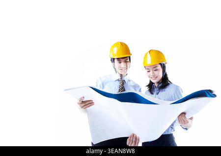 Two engineers in yellow hard hats review blueprints and discuss project details. Stock Photo