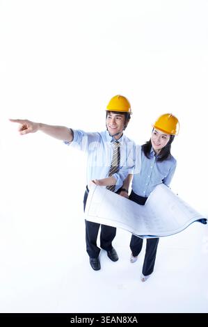 A team of engineers and architects, wearing hard hats, study blueprints and discuss construction plans. Stock Photo
