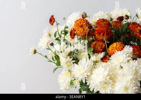 A white pitcher filled with orange and white flowers sits on a light surface. This setup can be used for home decoration or floral arrangement inspira Stock Photo