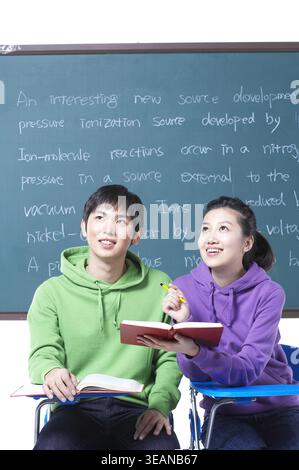 Two students studying together in front of a chalkboard full of chemistry notes. Stock Photo