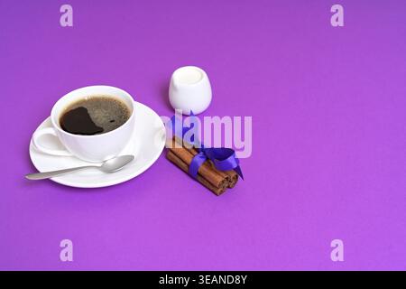 Cup of Black Coffee with Cinnamon Sticks and Milk Jug on Purple Background Stock Photo