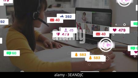 Writing child in yellow top wearing headset doing homework at home table, with laptop, pen, alerts. Student, remote, learning, screen, notebook, penci Stock Photo
