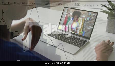 Reaching client in blue top adjusting charts at desk, laptop showing color wheel, currency overlay. Remote, studio, rack, wardrobe, palette, graphs, d Stock Photo
