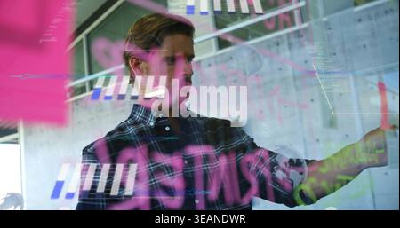 Pointing man wearing plaid shirt writing on glass board in modern workspace, pink data overlays. Brainstorming, collaboration, technology, interface, Stock Photo