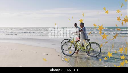 Walking pair pushing green bikes on beach barefoot prints waves gold-star overlay, copy space. Couple, cycles, footprints, ocean, stars, sunlit, outdo Stock Photo