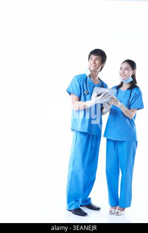 Two medical professionals in blue scrubs, holding a tablet and smiling, in a hospital setting. Stock Photo