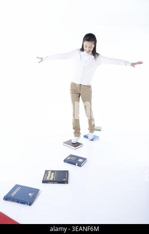 A young woman is balancing on a narrow path of books. Stock Photo
