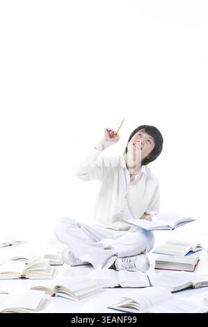 A young student sits on the floor surrounded by open books, lost in thought. Stock Photo