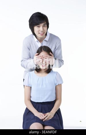 A man covers his girlfriend's eyes with his hands, smiling at her in a romantic gesture. Stock Photo