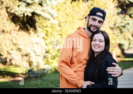 Young couple standing close together and hugging in park with trees and greenery in background. Concept of love and relationship. Stock Photo