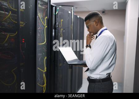 Technician, man or laptop with thinking in server room for console access, power backup or solution. IT engineer, black person and tech in data center Stock Photo