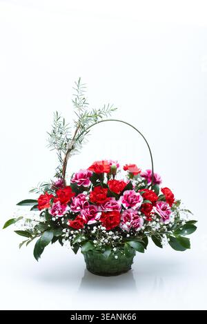 A beautiful bouquet of red and pink carnations, baby's breath, and greenery in a green wicker basket, arranged in a basket-style arrangement with a long handle. Stock Photo