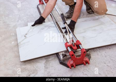 Worker cuts marble tiles using tile cutter during home renovation in building space. Stock Photo