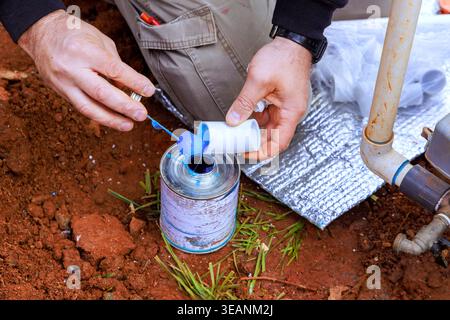 Worker stands in dirt, using adhesive blue glue of plastic pipe with water PVC Stock Photo