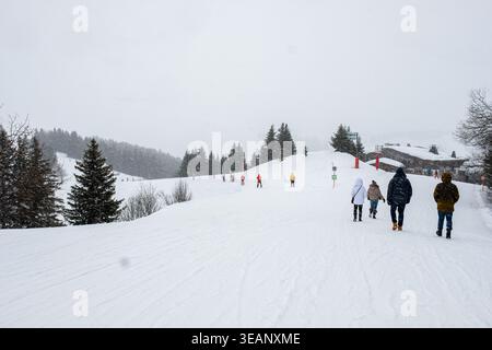 People walking through fresh snowfall on a snowy hillside with evergreen trees during a winter storm in Megeve, French Alps, France Stock Photo