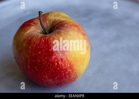 Fresh red and yellow apple with water droplets on a ceramic plate in soft natural light Stock Photo
