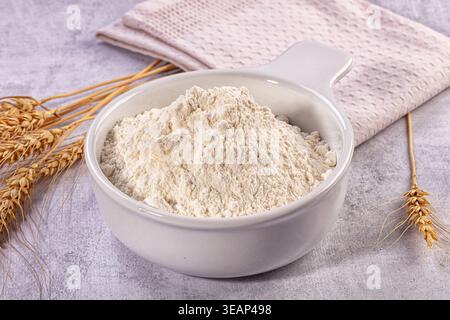 Close up still life image featuring ceramic bowl filled with fresh white flour, golden wheat stalks, folded light pink kitchen towel Stock Photo
