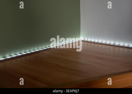 An LED lamp with an aluminum profile and a diffused plastic cover, mounted in the corner on a sage green and white wall. Stock Photo