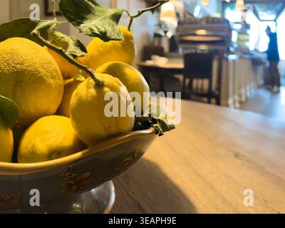 Citrus freshness on table, lemons in a bowl on wooden table inside cafe, creating bright natural accent and fresh food atmosphere, copy space Stock Photo