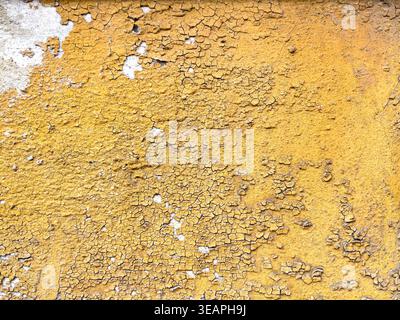 Sun altered painted wall shows cracked yellow surface, where exposure and material decay create granular patterns and uneven structure Stock Photo