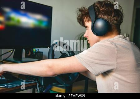 Young man playing racing video game with steering wheel and headset at home Stock Photo