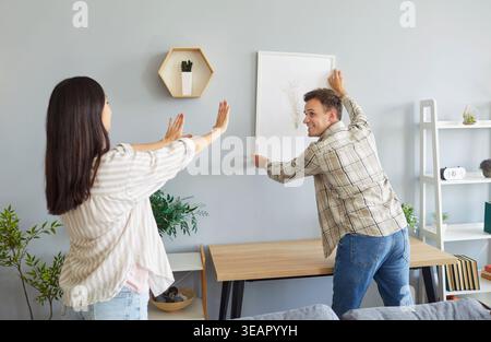 Happy couple decorating their house and hanging a picture on the wall in the living room Stock Photo